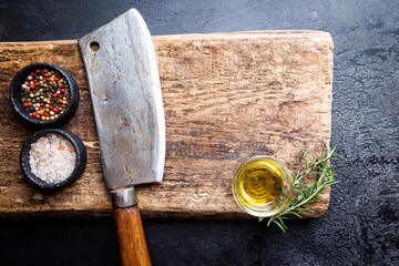 Cutting board, seasonings and oil set with meat cleaver on dark background, top view, copy space