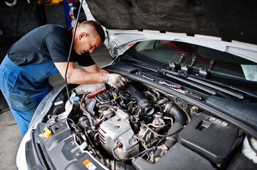 Car repair and maintenance theme. Mechanic in uniform working in auto service, checking engine.
