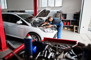 Fototapeta na wymiar Car repair and maintenance theme. Mechanic in uniform working in auto service, checking engine.