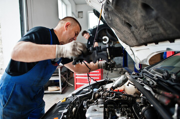 Car repair and maintenance theme. Mechanic in uniform working in auto service, checking engine.