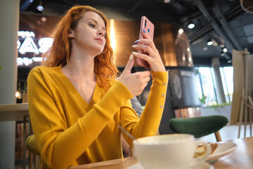 Portrait of smiling young woman sitting in cafe at center mall and using smartphone.