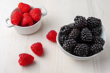 Top view of white bowl with blackberries and raspberries on white wooden table with raspberries, horizontal, with copy space