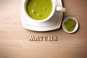 Japanese matcha green tea is poured into a white mug and on a white saucer in powder. Inscription in wooden letters in English. Tea set, invigorating drink, vigor, antioxidant. space for text
