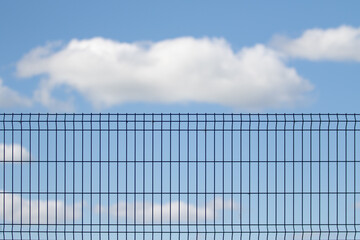 Metal grid against the blue sky with white clouds.