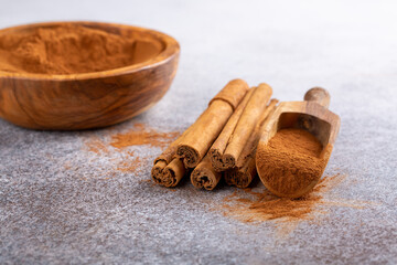 Ceylon cinnamon sticks with cinnamon powder in wooden bowl on concrete background. Copy space.