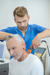 Bearded doctor performing ultrasound neck treatment on smiling mature patient