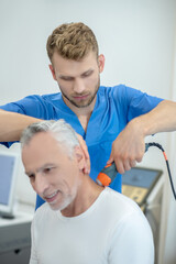 Obraz premium Bearded doctor performing ultrasound neck treatment on smiling mature patient