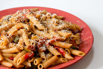 Penne rigate pasta with courgettes, bacon and tomatoes, sprinkled with parmesan cheese
