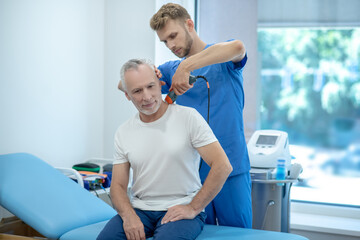 Obraz premium Mature patient sitting on coach, receiving ultrasound treatment of his neck