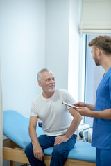 Obraz premium Young bearded doctor showing clip folder to mature male patient