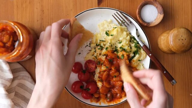 Scrambled eggs and baked beans breakfast. Woman eating omelette scrambled eggs with baked beans and toasts for breakfast, top view