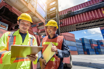 Engineer men wearing yellow hardhat standing near forklift cargo at the container yard and check for control loading Containers box from Cargo freight ship for import and export. Teamwork concept