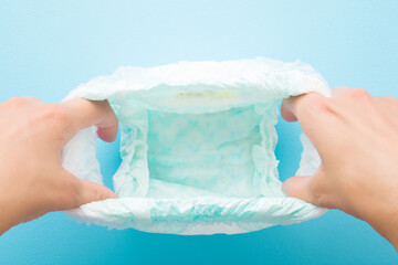 Young mother hands showing opened white baby diaper pants on light blue table background. Pastel...