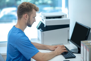 Obraz premium Young adult man in medical uniform sitting at computer