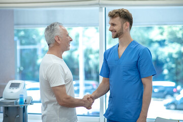 Elderly man and young doctor shaking hands