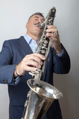 Fototapeta premium A man, dark, short hair, plays the bass clarinet. Studio, light background