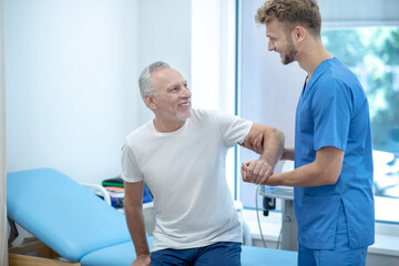 Fototapeta premium Young doctor helping patient to sit on couch