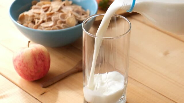 Pouring milk in a glass on wooden table. Breakfast food. Slow motion of milk pour in glass
