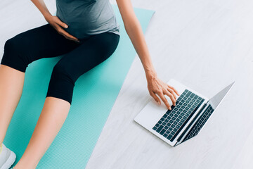 Cropped view of pregnant woman using laptop on fitness mat at home