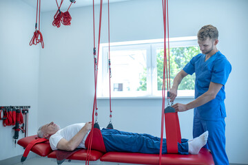 Elderly man lying on couch and physician rehabilitologist