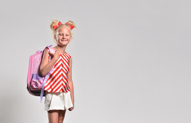 Schoolgirl with backpack on gray background in red striped clothes