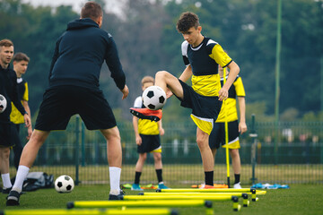Fototapeta Teenagers on soccer training camp. Boys practice football witch young coaches. Junior level athletes improving soccer skills on outdoor training. Player kick soccer ball to coach and ladder skipping obraz
