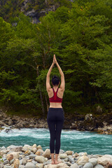 Yoga classes in nature. The concept of playing sports alone. Social exclusion. A woman does yoga on rocks, near a mountain river flows