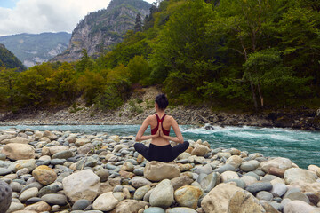 Fototapeta na wymiar Yoga classes in nature. The concept of playing sports alone. Social exclusion. A woman does yoga on rocks, near a mountain river flows