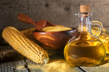 Corn grits polenta and corn oil in a bottle, corn groats and corncobs on wooden rustic table. The concept of healthy eating and nutrition. Vintage style composition.