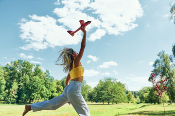 Beautiful young woman running in the park while playing with toy airplane on a sunny day outdoor....