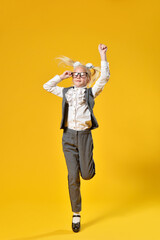 Active girl child of preschool age jumping on yellow background