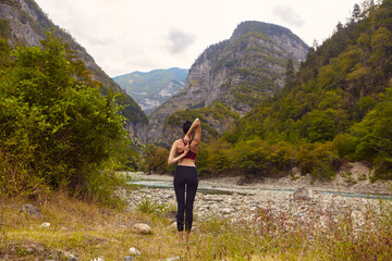 Naklejka na ściany i meble Yoga classes in nature. The concept of playing sports alone. Social exclusion. A woman does yoga on rocks, near a mountain river flows