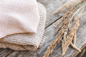 Autumn or winter background. Stack of cozy knitted wool clothes sweaters and dried plant on wooden table. Hygge mood, cold weather concept. Handmade knitted sweaters.