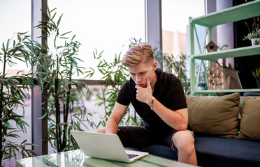 Young freelance guy working on a laptop while sitting at a table in the cafeteria