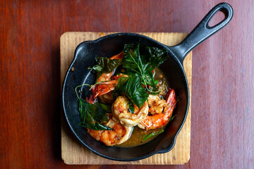 Spicy large prawns served on a frying pan with fresh herbs on a wooden table.