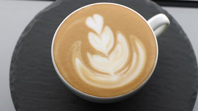 white coffee cup with rosetta latte art rotating on a black stone background, template for summer drink menu of cafe and restaurant
