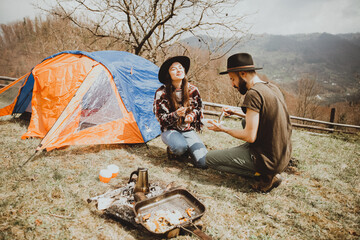 Loving couple sitting on the mountain outdoors. Man and woman travel together. Couple traveler enjoys nature, hugs, looks at the landscape near the tent