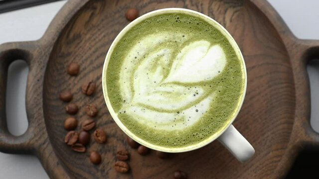 white coffee cup with green matcha latte art and coffee beans on a wooden plate top view. template for summer drink menu of cafe and restaurant
