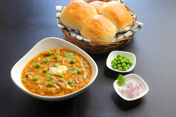 Indian Mumbai Street style Pav Bhaji, garnished with peas, raw onions, coriander, and Butter. Spicy thick curry made of out mixed vegetables served with paav over black background with copy space. 