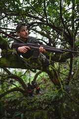 Soldier or revolutionary member or hunter in camouflage on the tree observing the gun in his hand