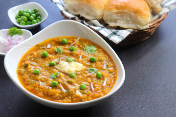 Indian Mumbai Street style Pav Bhaji, garnished with peas, raw onions, coriander, and Butter. Spicy thick curry made of out mixed vegetables served with paav over black background with copy space. 