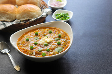 Indian Mumbai Street style Pav Bhaji, garnished with peas, raw onions, coriander, and Butter. Spicy thick curry made of out mixed vegetables served with paav over black background with copy space. 