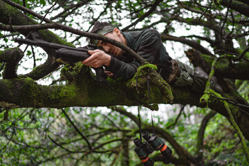 Soldier or revolutionary member or hunter in camouflage on the tree aiming the gun in his hand, hunter concept
