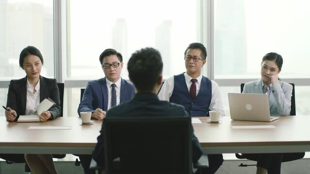 rear view of a young asian businessman being interviewed by a group of HR executives in conference room of modern corporation