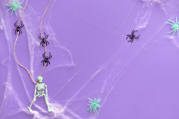 Minimal Halloween background with hung skeleton, spider web and line of black spiders on vibrant purple neon paper. Top view, trendy background.