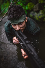 Fototapeta na wymiar Soldier or revolutionary member or hunter aiming with gun in his hand in camouflage in the river, hunt concept