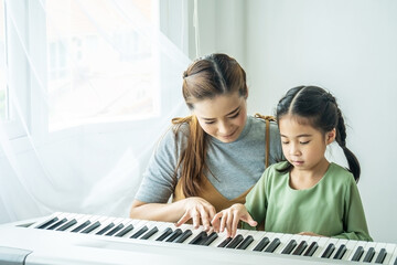 Happy little Asian deaughter playing piano with mother at home, Mother teaching daughter to play...