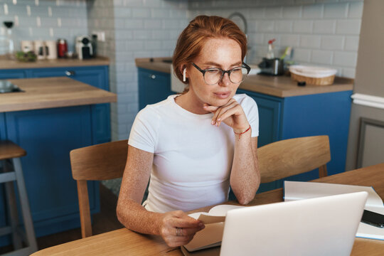 Image of focused ginger woman in earphones working with laptop