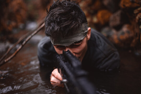 Soldier or revolutionary member or hunter aiming with gun in his hand in camouflage in the river, hunt concept