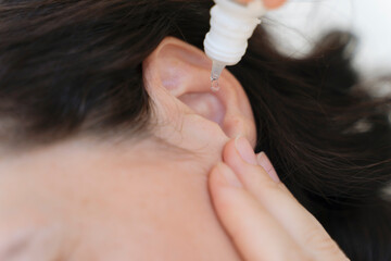Medical pipette with a drop of medication over the patient's ear. Ear diseases